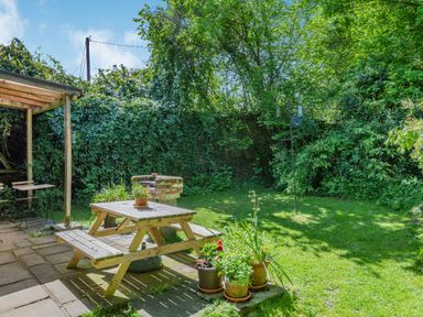A garden with a wooden picnic table and potted plants next to a covered patio and brick barbecue at Endymion in Linwood near Ringwood New Forest