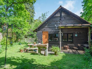A garden area with a wooden picnic table and a small table with two chairs by a wooden building at Endymion Linwood near Ringwood New Forest