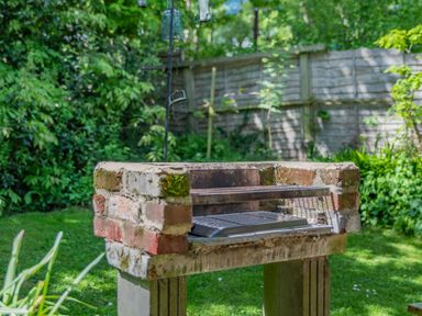 A brick and concrete barbecue grill in a garden with green plants and a wooden fence in the background at Endymion in Linwood near Ringwood New Forest