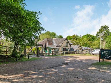 An outdoor view of a building with signs for High Corner Inn and a gravel parking area with green trees surrounding at Endymion Linwood near Ringwood New Forest