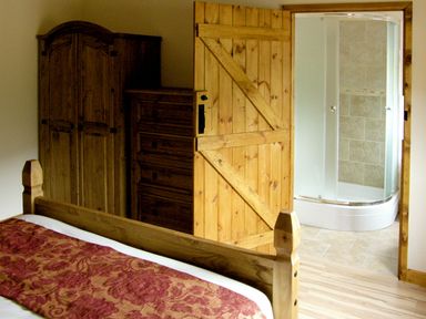 A bedroom with a bed a wooden wardrobe a chest of drawers and an open wooden door leading to a bathroom with a shower at Happy Union Stables in Abbeycwmhir near Rhayader