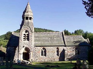 A stone church with a tall steeple and arched windows in a green landscape at Happy Union Stables Abbeycwmhir near Rhayader