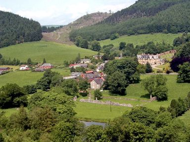 A rural landscape with green fields trees hills and a small village with houses and farm buildings at Happy Union Stables in Abbeycwmhir near Rhayader