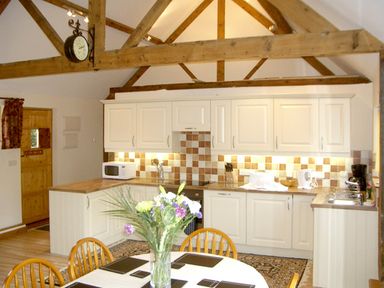 A kitchen with wooden beams white cabinets a dining table with flowers and wooden chairs at Happy Union Stables in Abbeycwmhir near Rhayader