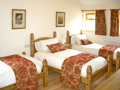 A bedroom with three single beds with red patterned bed runners and cushions at Happy Union Stables in Abbeycwmhir near Rhayader