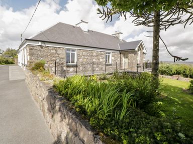 An exterior view of a stone house with a slate roof and a garden with plants and a tree at Prague House in Lettermore County Galway
