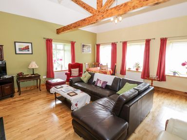 A living room with a leather sofa a red armchair wood beams and a dining table at Prague House in Lettermore County Galway