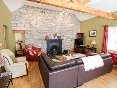 A living room with stone wall fireplace brown leather sofa red and cream armchairs wooden furniture and green walls at Prague House in Lettermore County Galway