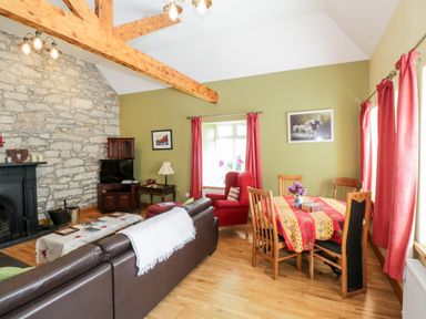 A living room with a stone fireplace wooden beams red curtains and a dining table with chairs at Prague House in Lettermore County Galway