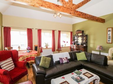 A living room with a sectional sofa armchairs a wooden dining table with chairs and an antique cabinet at Prague House in Lettermore County Galway