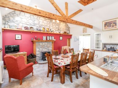 A dining room with a large wooden table and chairs a red armchair a stone fireplace and wooden ceiling beams at Prague House in Lettermore County Galway