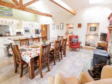 A kitchen and dining area with a wooden table and chairs a red armchair a stove and wooden beams on the ceiling at Prague House in Lettermore County Galway
