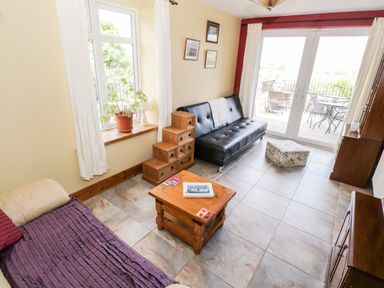 A sitting room with sofas a wooden coffee table a plant on a windowsill and glass doors leading outside at Prague House in Lettermore County Galway