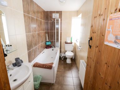 A bathroom with a bathtub a toilet and a sink with towels on the sink and a wooden door at Prague House in Lettermore County Galway