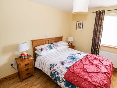 A bedroom with a wooden bed and two bedside tables with lamps and floral bedding at Prague House in Lettermore County Galway