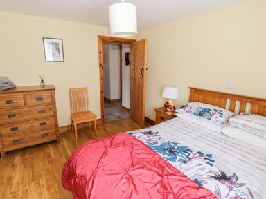 A bedroom with a wooden bed with floral bedding a wooden dresser a wooden chair and a lamp at Prague House in Lettermore County Galway