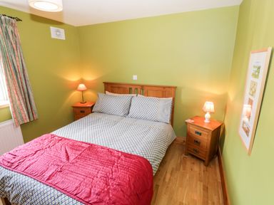 A bedroom with a wooden double bed red blanket two wooden nightstands with lamps green walls and wooden floor at Prague House in Lettermore County Galway