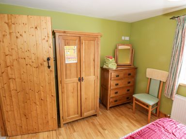 A bedroom with wooden wardrobe dresser chair and window at Prague House in Lettermore County Galway