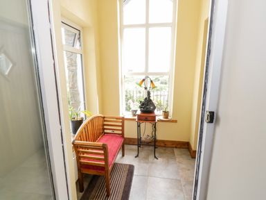 A small seating area with a wooden bench with a red cushion a table with a lamp and plants in front of a window at Prague House in Lettermore County Galway