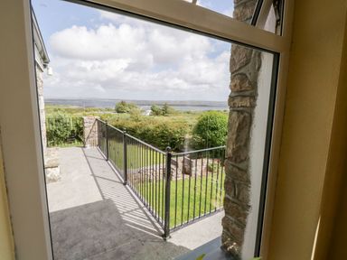 A balcony with black metal railing overlooking a garden and distant water at Prague House in Lettermore County Galway