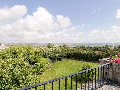 A garden with green bushes and lawn with a view of water and houses in the distance at Prague House in Lettermore County Galway