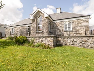 A stone house with a slate roof and a black metal railing on a grassy lawn at Prague House in Lettermore County Galway