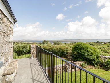 A stone balcony with a black metal railing overlooking green bushes and a distant body of water at Prague House in Lettermore County Galway