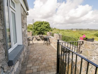An outdoor patio with stone walls metal railings tables and chairs overlooking greenery and fields at Prague House in Lettermore County Galway