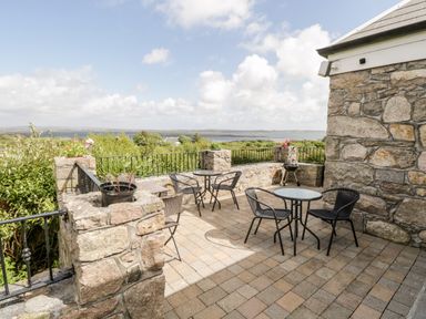 An outdoor patio with stone walls tables and chairs overlooking vegetation and water at Prague House in Lettermore County Galway