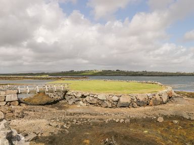 A stone wall enclosing grass and a small wooden bridge over rocky ground near water at Prague House in Lettermore County Galway
