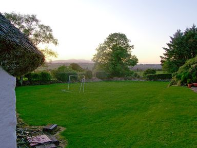 A garden with a small soccer goal surrounded by trees and a thatched roof building at Carthy's Cottage Kilbrien near Dungarvan County Waterford