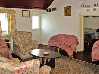 A living room with floral upholstered armchairs a wooden coffee table and a small sofa with a pink cover at Carthys Cottage in Kilbrien near Dungarvan County Waterford