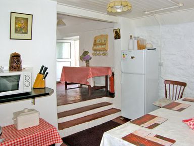 A kitchen with a microwave knife block and fridge with tables covered with checkered and white tablecloths at Carthy's Cottage Kilbrien near Dungarvan County Waterford