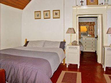 A bedroom with a bed and two nightstands with lamps and a view into a second room with a dresser at Carthy's Cottage Kilbrien near Dungarvan County Waterford