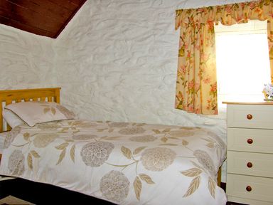 A bedroom with a single bed with floral bedding and a chest of drawers next to a window with floral curtains at Carthy's Cottage Kilbrien near Dungarvan County Waterford