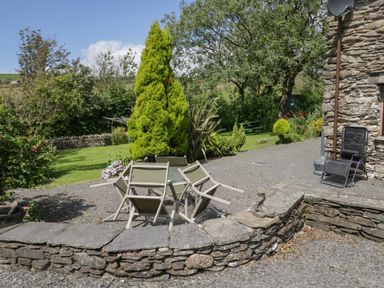 An outdoor garden area with a stone wall surrounding overturned patio chairs and various plants at Woodside Barn in Pennington near Ulverston