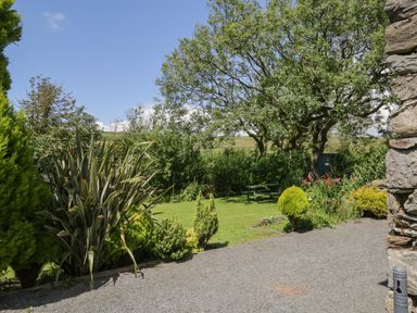 A garden with various plants trees and a green picnic bench at Woodside Barn in Pennington near Ulverston
