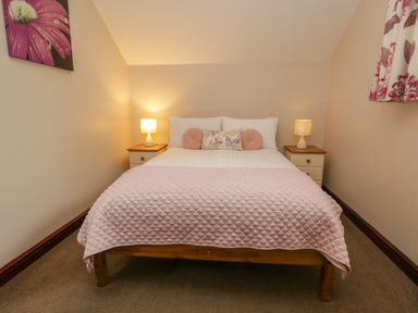 A bedroom with a double bed with pink quilt and cushions two bedside tables with lamps and floral artwork on the wall at Woodside Barn in Pennington near Ulverston