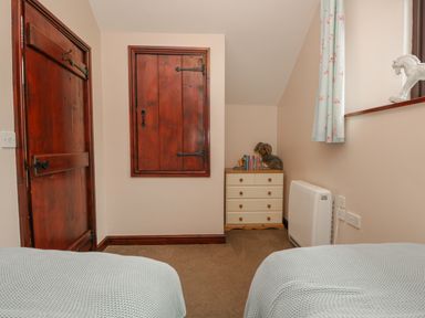 A bedroom corner with a wooden door and cabinet a chest of drawers with books and toys and a window with floral curtains at Woodside Barn Pennington near Ulverston