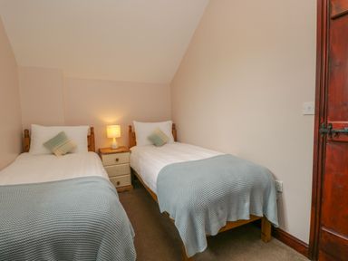 A bedroom with two single beds a bedside table with a lamp and a wooden door at Woodside Barn in Pennington near Ulverston