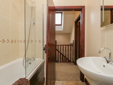 A bathroom with a bathtub shower and sink overlooking a staircase through an open door at Woodside Barn in Pennington near Ulverston