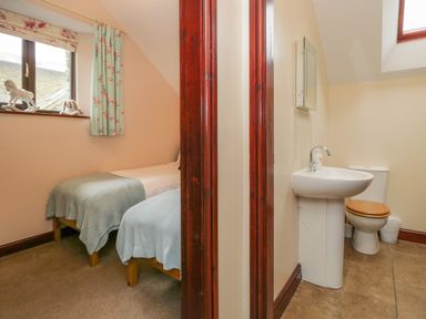 A bedroom with two single beds and a window adjacent to a bathroom with a sink and toilet at Woodside Barn in Pennington near Ulverston