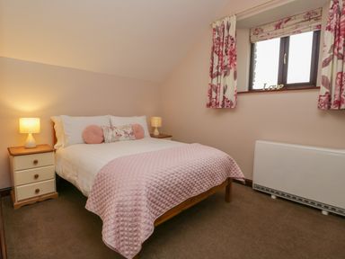 A bedroom with a bed pink bedding and pillows two bedside tables with lamps and a window with floral curtains at Woodside Barn in Pennington near Ulverston
