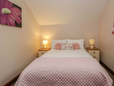 A bedroom with a double bed with pink and white bedding and two bedside tables with lamps at Woodside Barn in Pennington near Ulverston