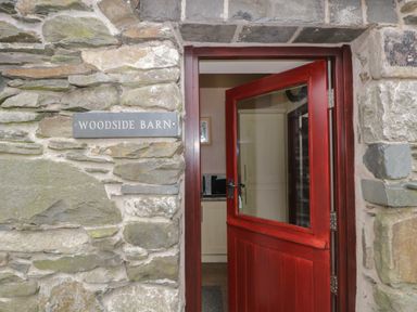 A red half-glass door open on a stone wall with a sign reading Woodside Barn Pennington near Ulverston