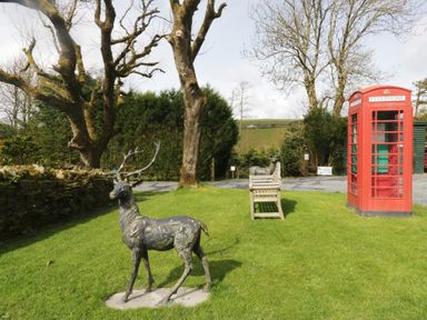 A deer statue, bench, and telephone box in a garden at Woodside Barn Pennington near Ulverston