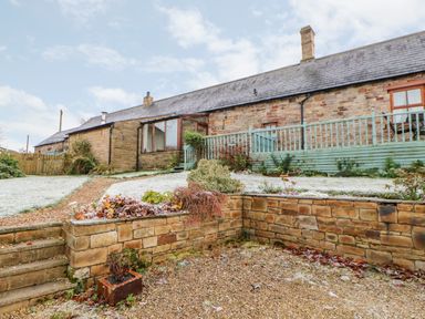 A stone house with a sloped roof and fenced porch with garden beds and gravel pathways at The Stable in Milton near Brampton