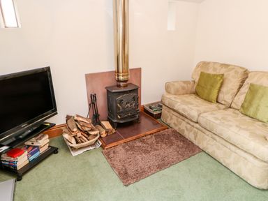 A living room with a wood stove and firewood next to a sofa and a television at The Stable in Milton near Brampton