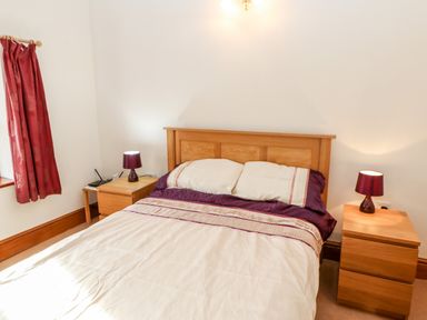 A bedroom with a double bed wooden headboard bedside tables with lamps and red curtains at The Stable in Milton near Brampton
