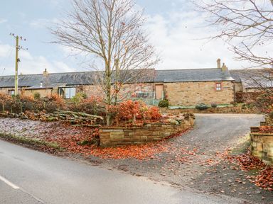 A stone cottage with a driveway and autumn leaves on the ground at The Stable in Milton near Brampton